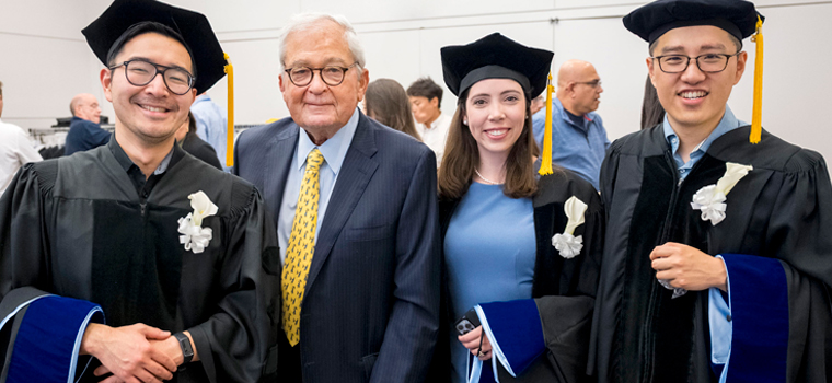 A group of smiling students in graduation caps and gowns stand alongside Louis V. Gerstner, Jr. 