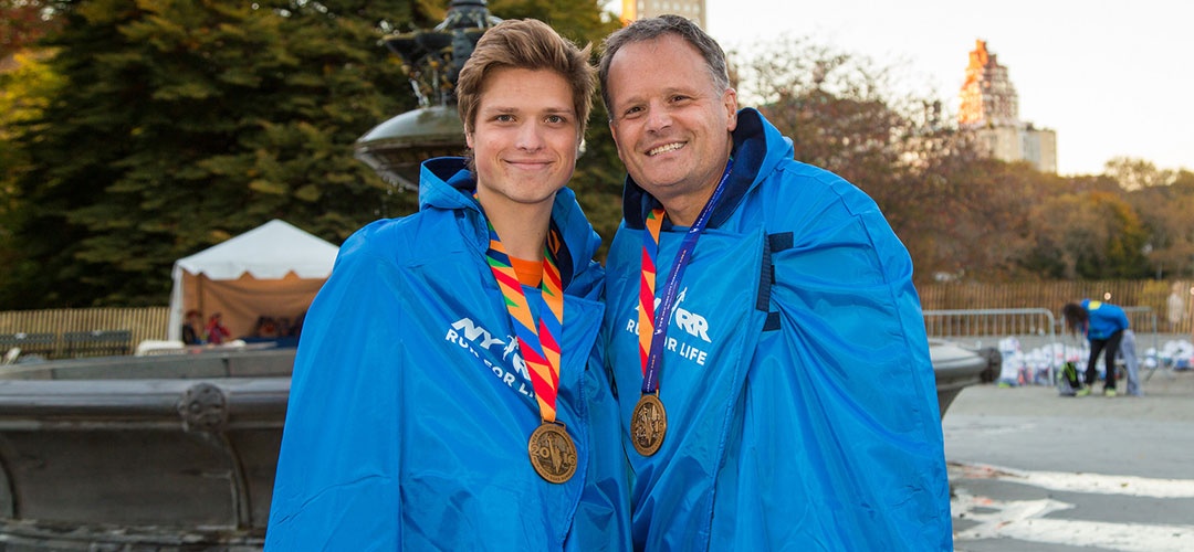 Sam and his father after NYC Marathon wearing blue jackets and medals around neck
