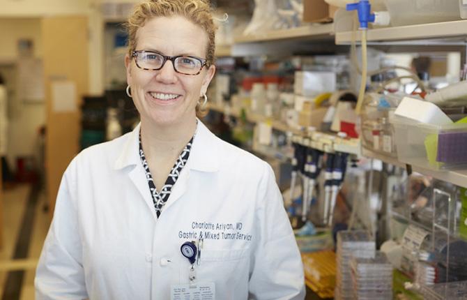 An MSK scientist wearing a lab coat looks at the camera smiling.