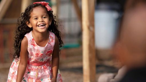 A young girl in a pink dress stands and laughs.